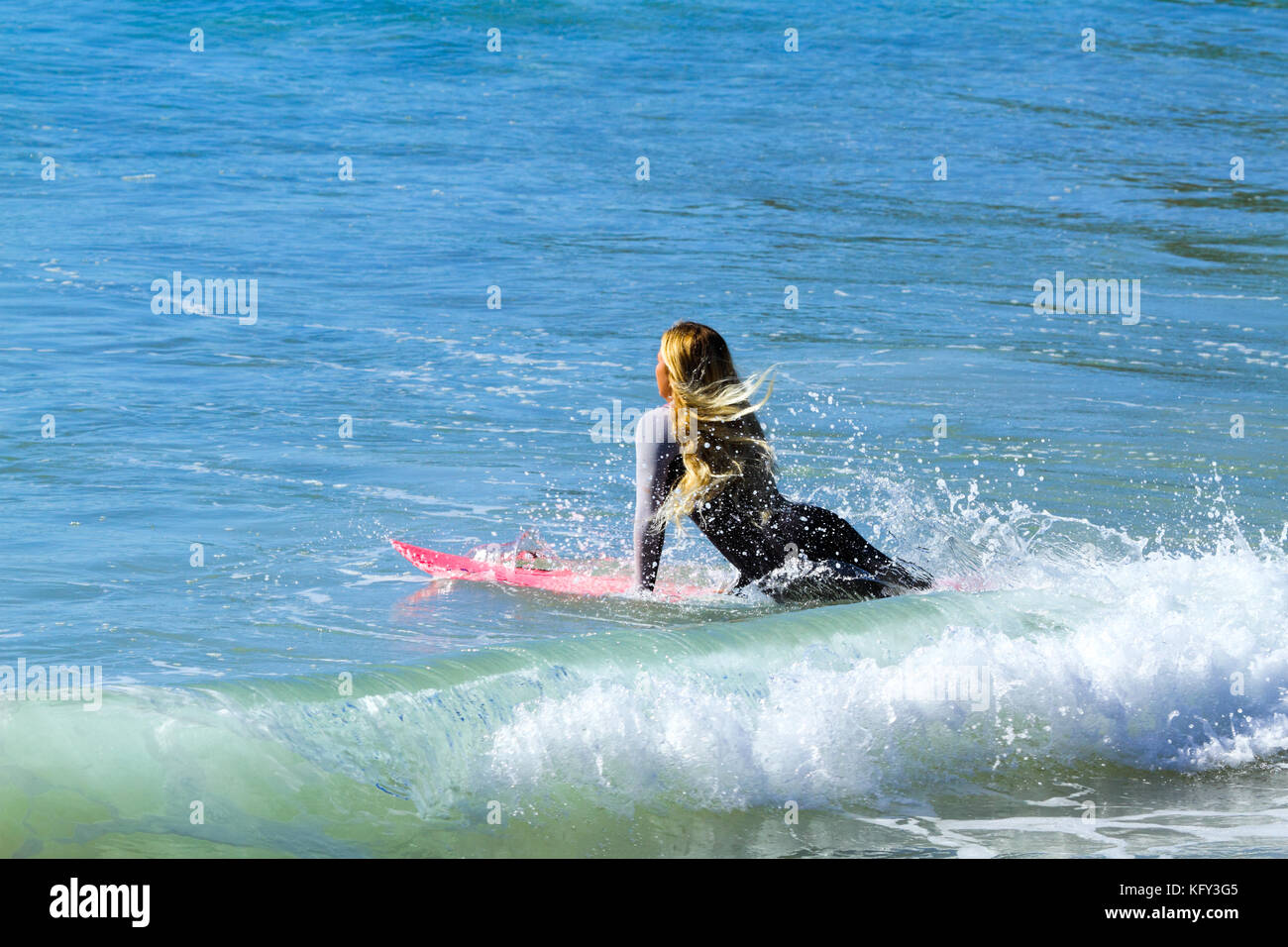 A blond lady in her early twenties wades into the surf with surfboard Stock Photo