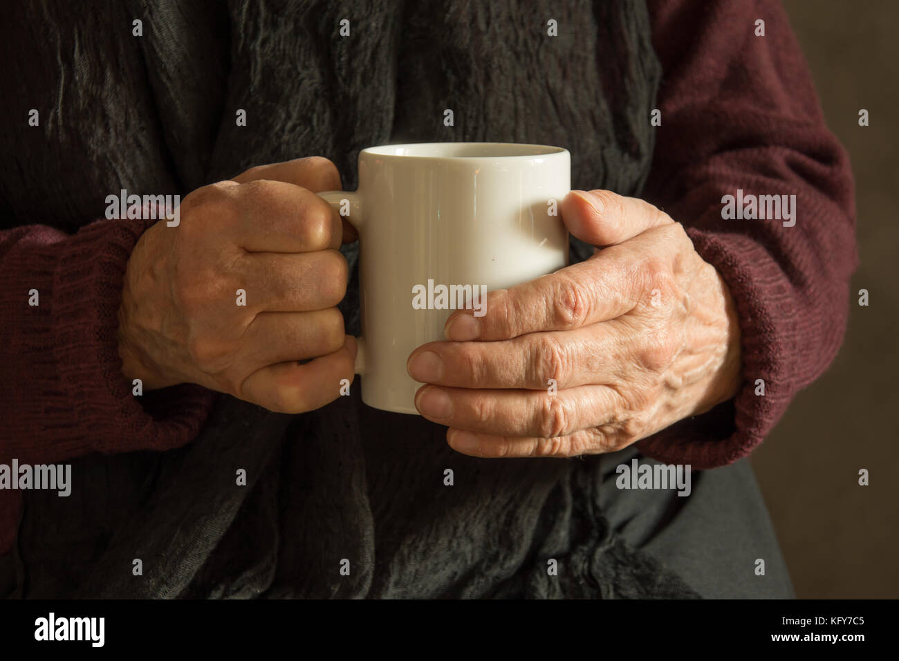 Old woman's wrinkled hands holding a mug with a drink - closeup Stock Photo