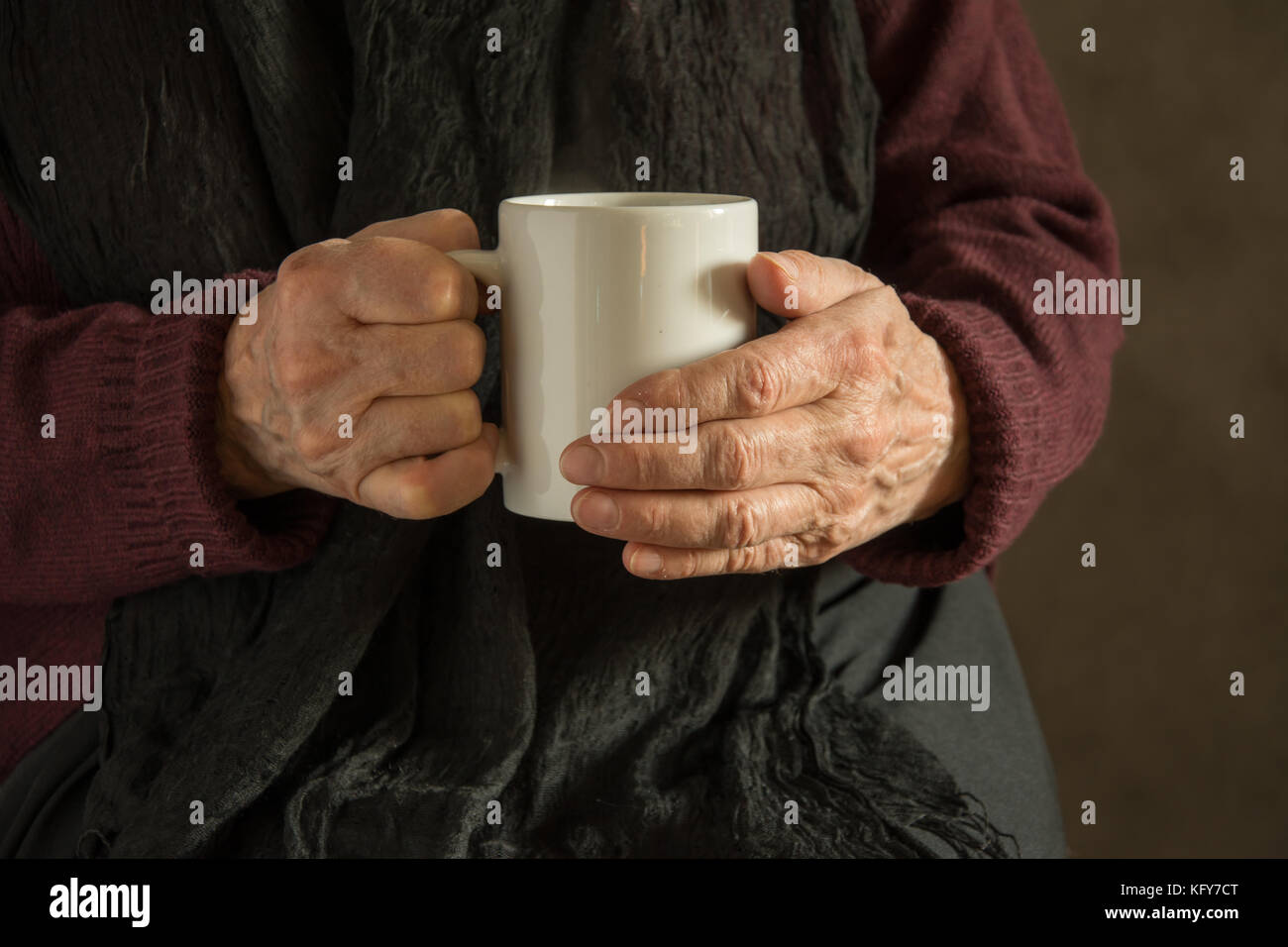 Old woman's wrinkled hands holding a mug with a drink Stock Photo