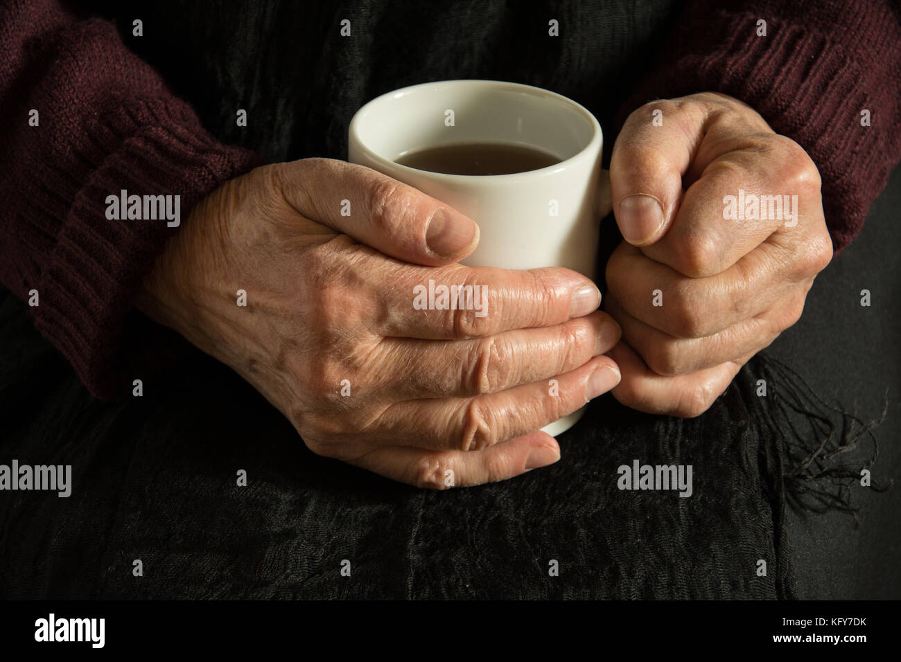 Old woman warming her wrinkled hands with a mug of coffee Stock Photo