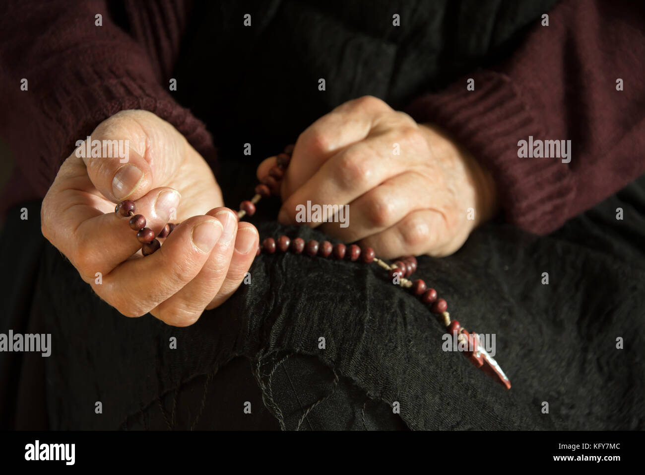 Hands of an old woman praying with a rosary Stock Photo