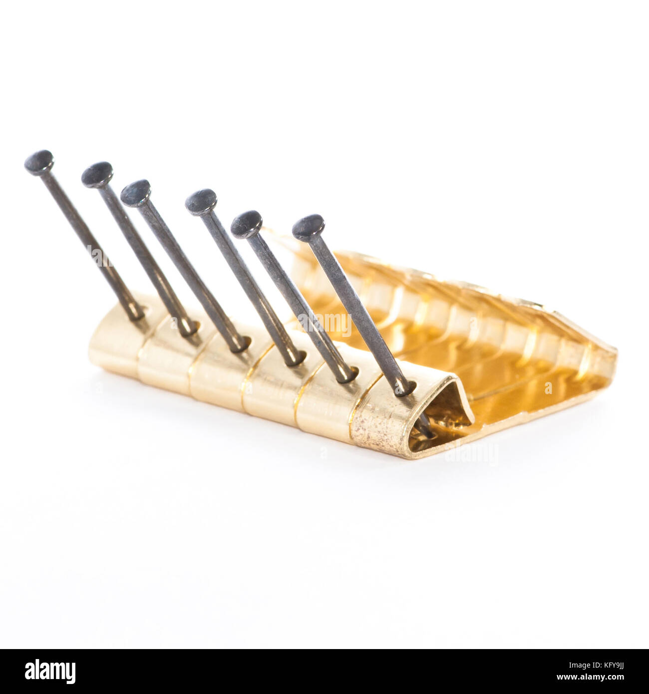 A row of brass picture hooks and nails shot against a white background. Stock Photo