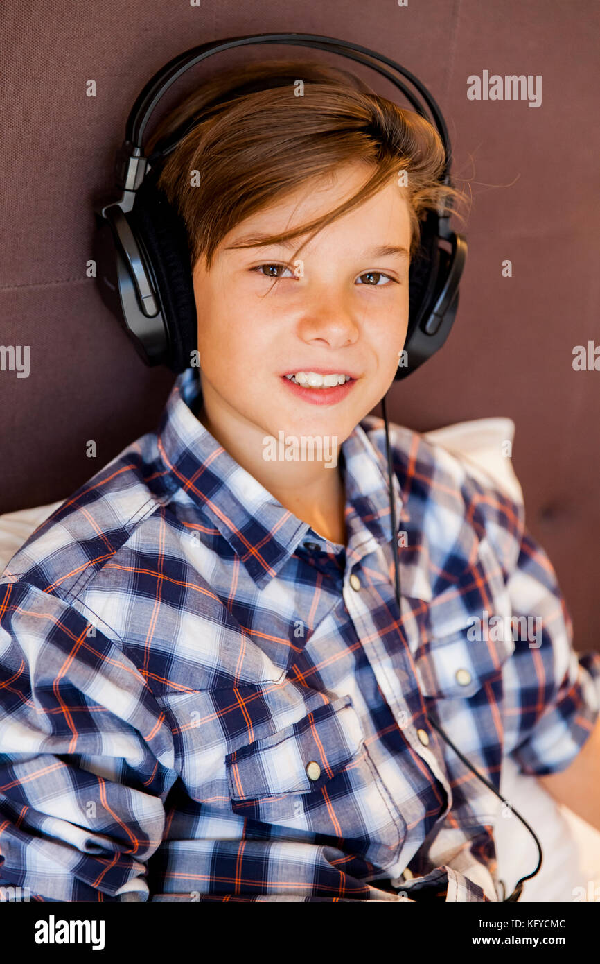 Portrait of teen boy listening music from earphones in bed Stock Photo
