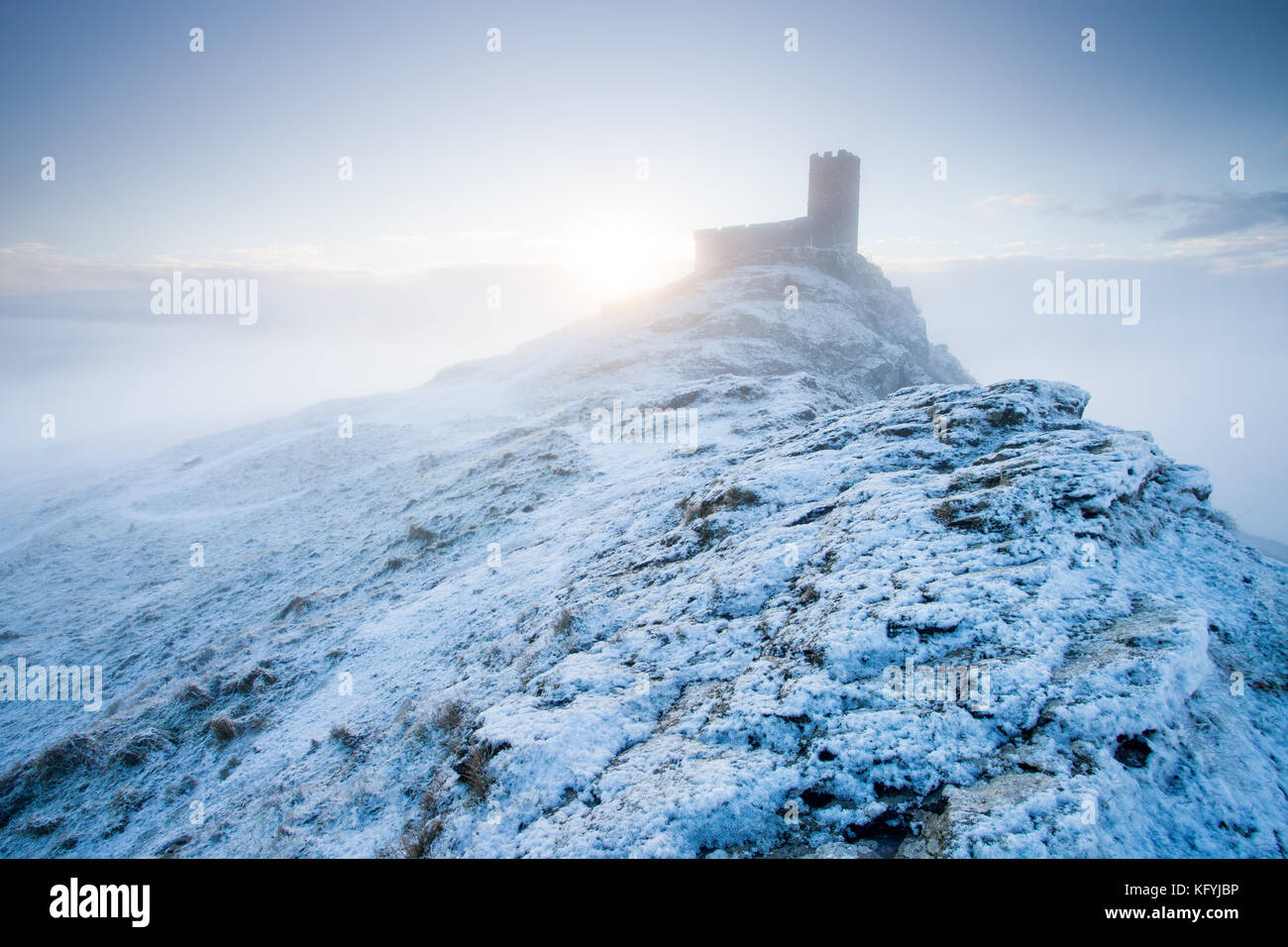 Sun rising from behind the small church of St Michael de Rupe, perched on top of Brentor, Dartmoor National park, England Stock Photo