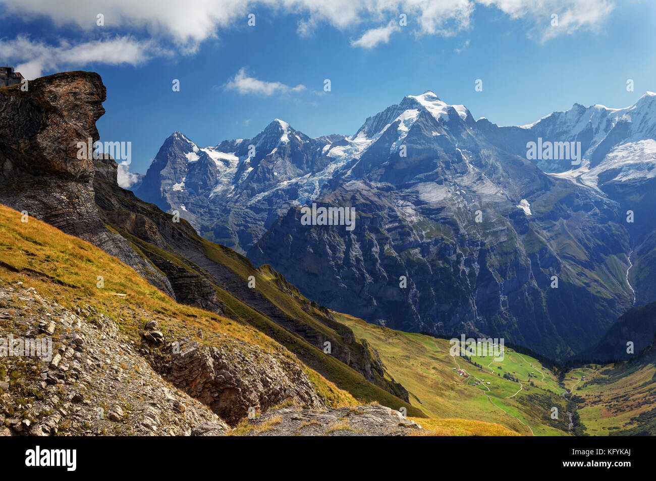 Looking down meadow on Schilthorn mountain, villages of Schiltalp and Gimmeln below, Eiger, Mönch and Jungfrau in background, Switzerland Stock Photo