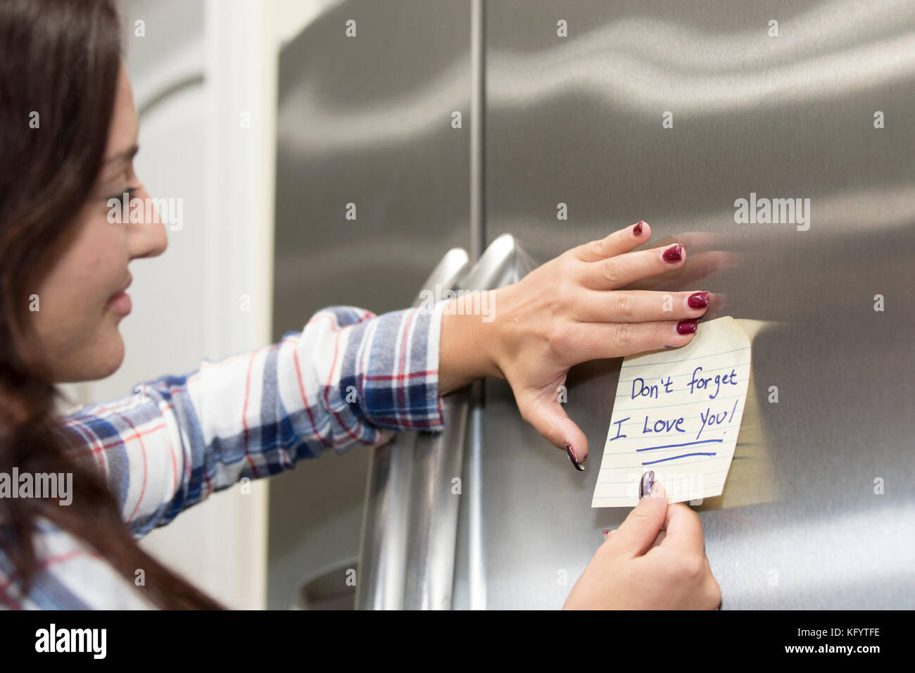 Attractive 20-25 year old female sticking a love note on the refrigerator. Stock Photo