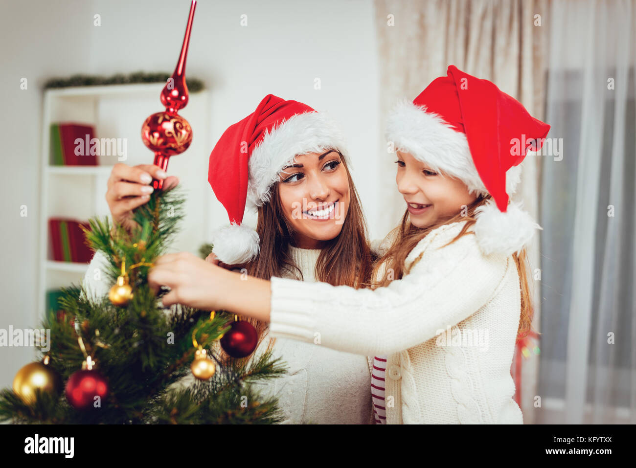 Beautiful happy little girl decorating Christmas tree with her mother ...