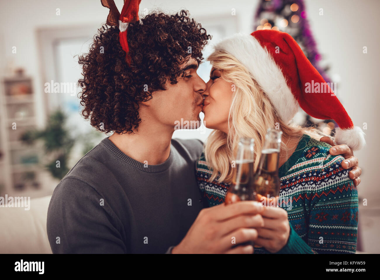 Young romantic couple hugging and kissing in Christmas time. They are toasting with bottles of drink. Stock Photo