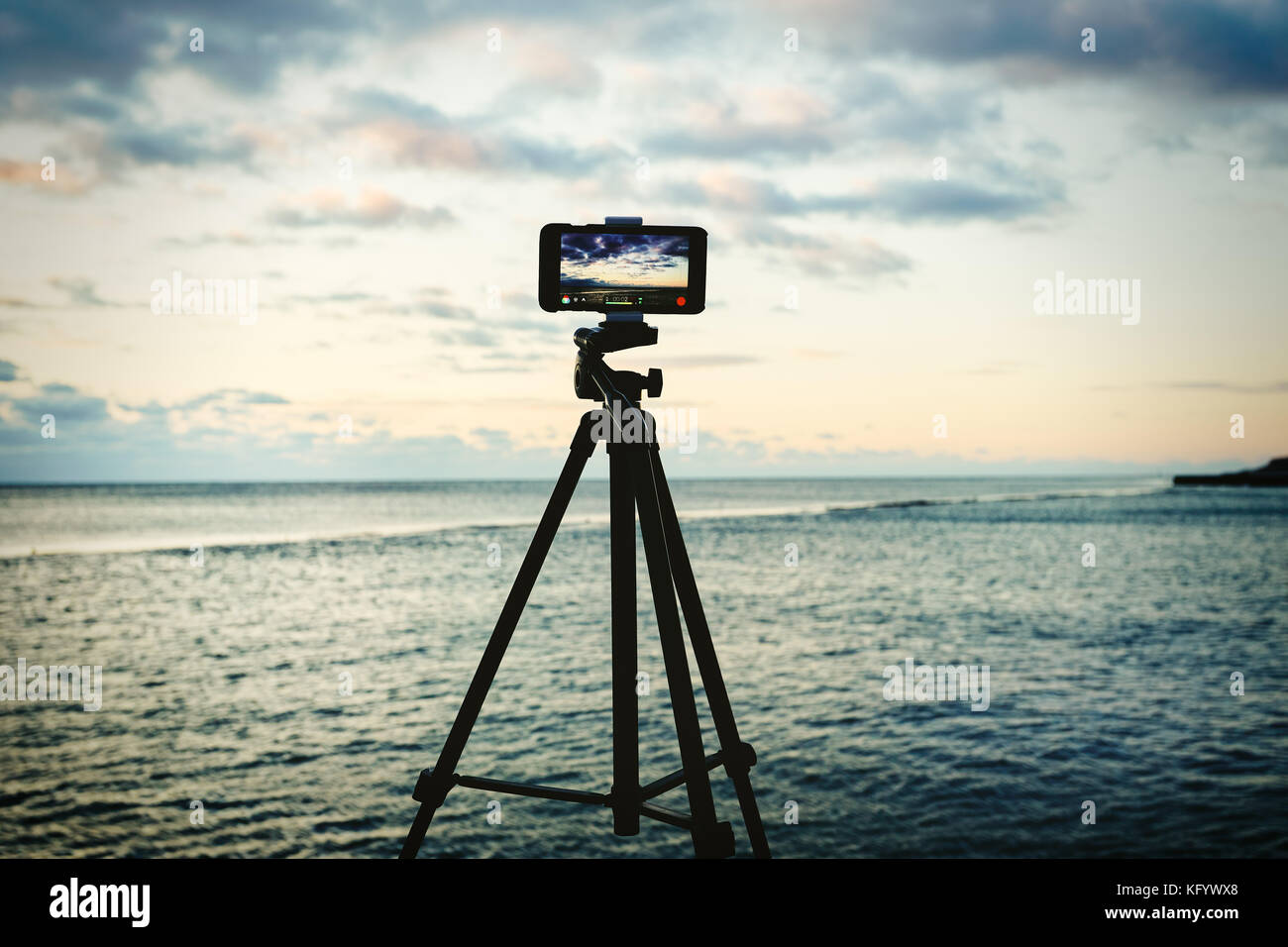 Smartphone on tripod capturing seascape sunrise. Mobile photography or videography concept. Stock Photo