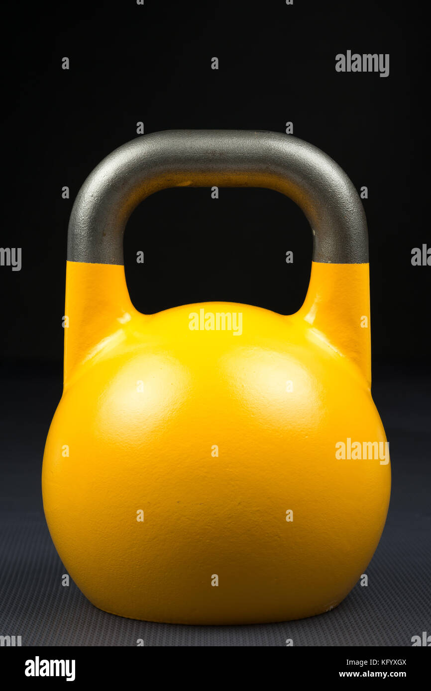 Single yellow competition kettlebell on a weight training gym floor. Potential text / writing space on and above kettlebell. Stock Photo