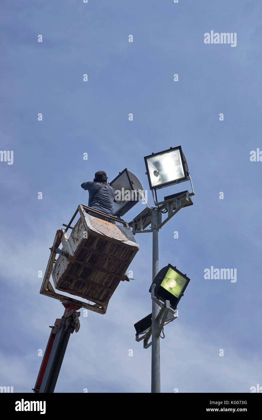 Man using an elevated crane jib to repair overhead light. Stock Photo