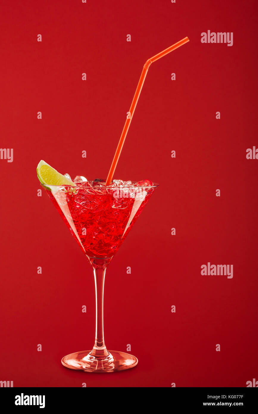 glass with red cocktail, lemon slice, ice cubes and thin cane on red