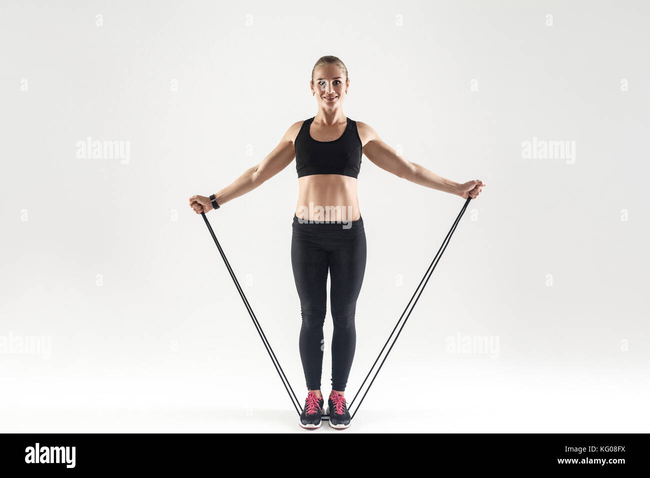 TRX training. Activity happiness woman holding skipping rope, toothy smiling and looking at camera. Studio shot, gray background Stock Photo