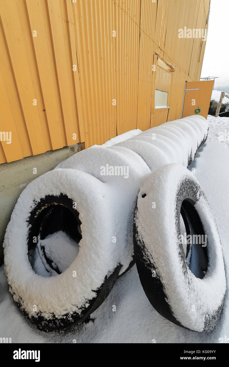 Old yellow wooden port warehouse-row of old tires for making pneumatic fenders-dock bumpers stored on the gangplank-pier on the N.side of the fishing  Stock Photo