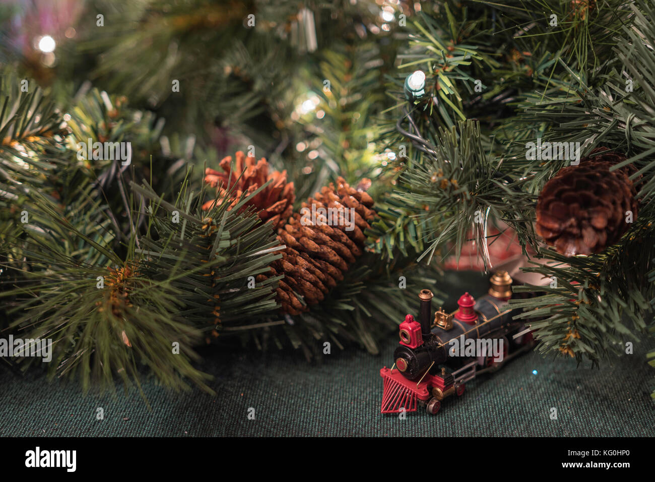 Christmas display with a small toy train surrounded by greenery and pine cones with white twinkle lights Stock Photo