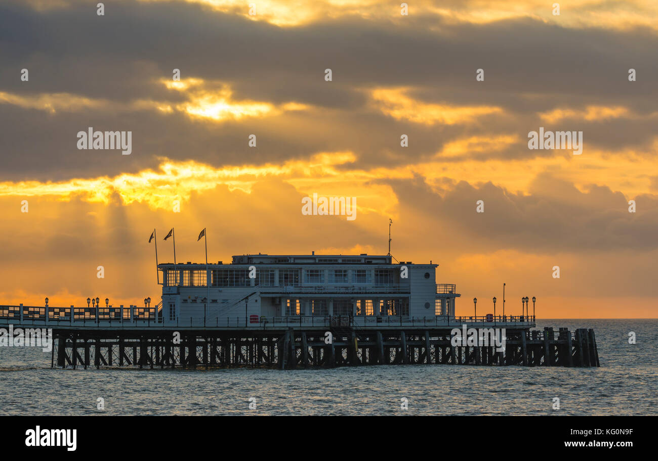 Sun rising with the suns rays shining through clouds on a cloudy morning at Worthing Pier in Worthing, West Sussex, England, UK. Stock Photo