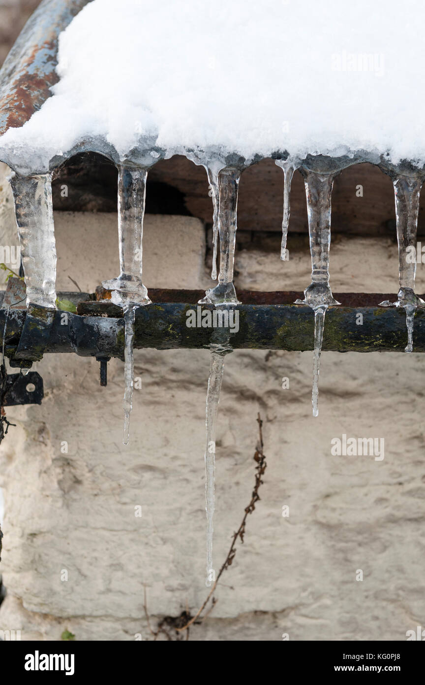 UK. Winter on the Welsh borders. Icicles on a corrugated iron roof and an old cast iron gutter Stock Photo
