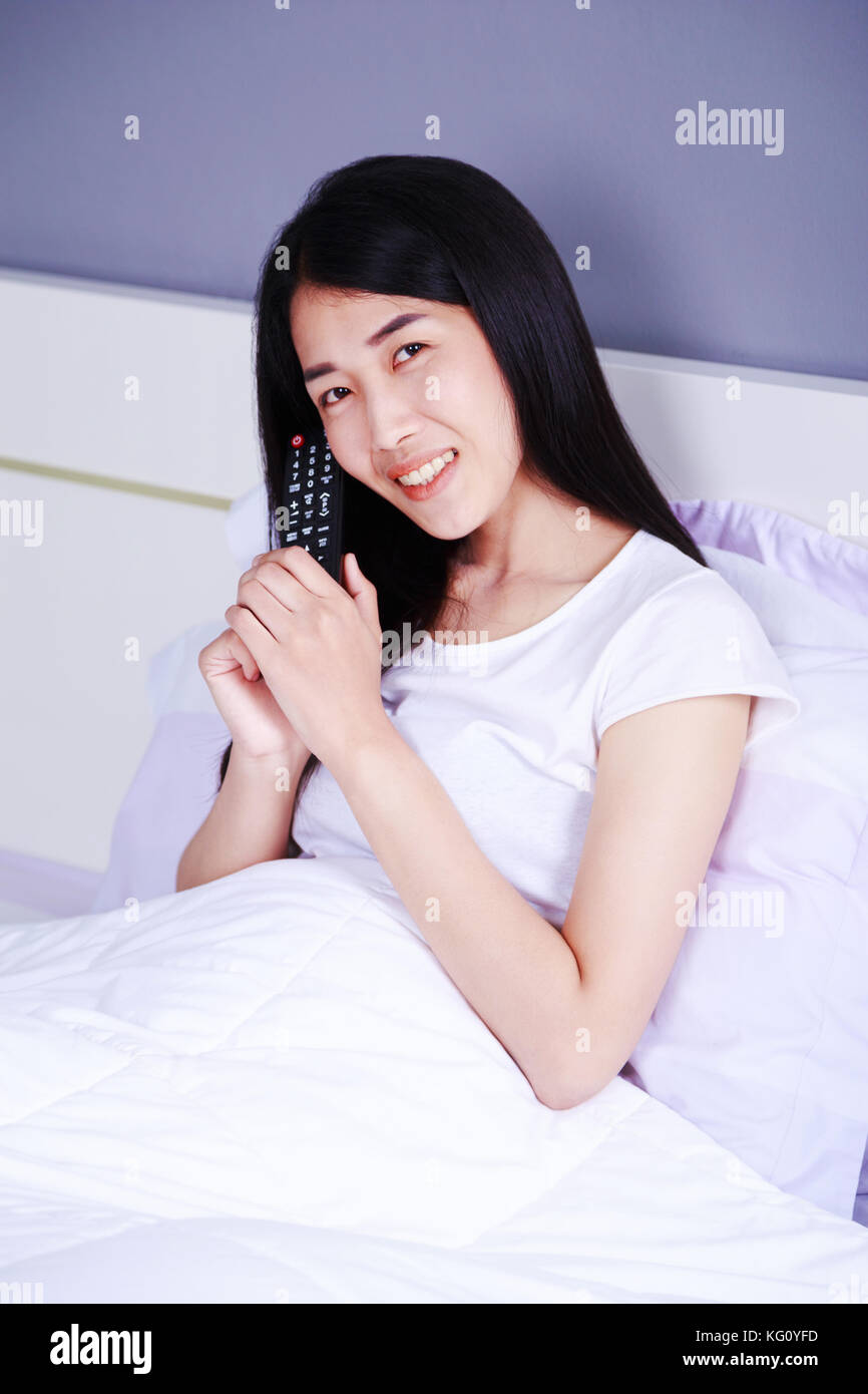smilling woman with tv remote control on bed in the bedroom Stock Photo