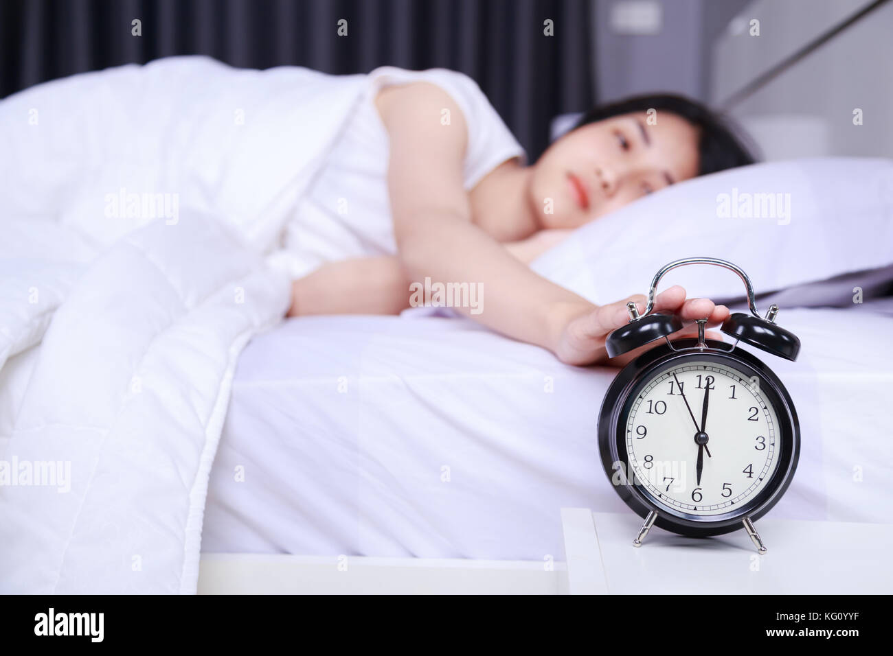 woman sleeping on bed and rise hand to turn off alarm clock in the