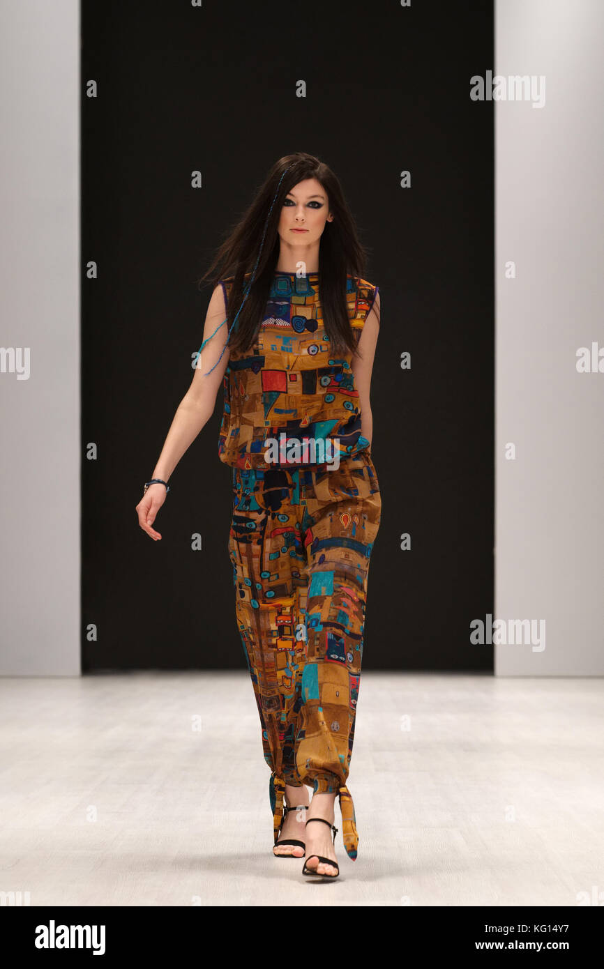 Fashion model in silk dress with ethnic ornament walking on podium during fashion week show. Stock Photo
