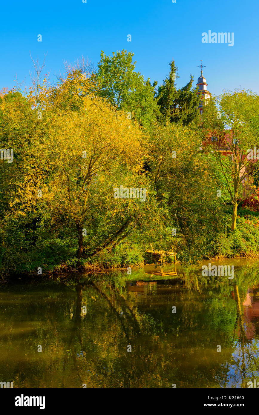 Colorful scenic idyllic autumn landscape at a river shore with trees reflecting on the water on a sunny autumn day with blue sky and an old church Stock Photo