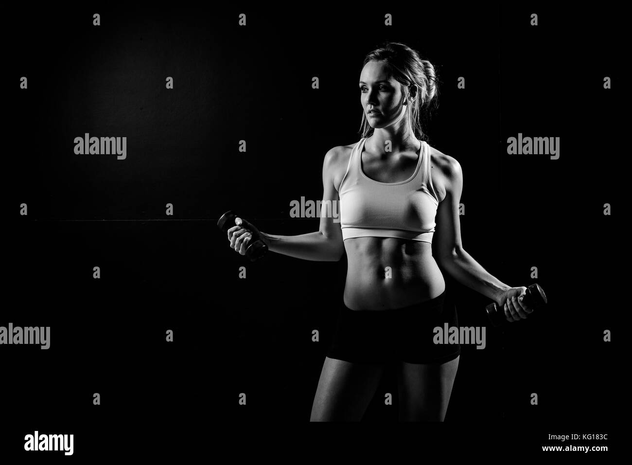 Beautiful female fitness model holding her towel/weights in a dark