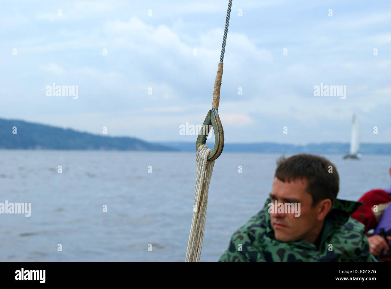 View from the side of a sailing boat. In the foreground in focus - a tight shroud with eye splice. The middle plan is the slightly blurred face of the Stock Photo