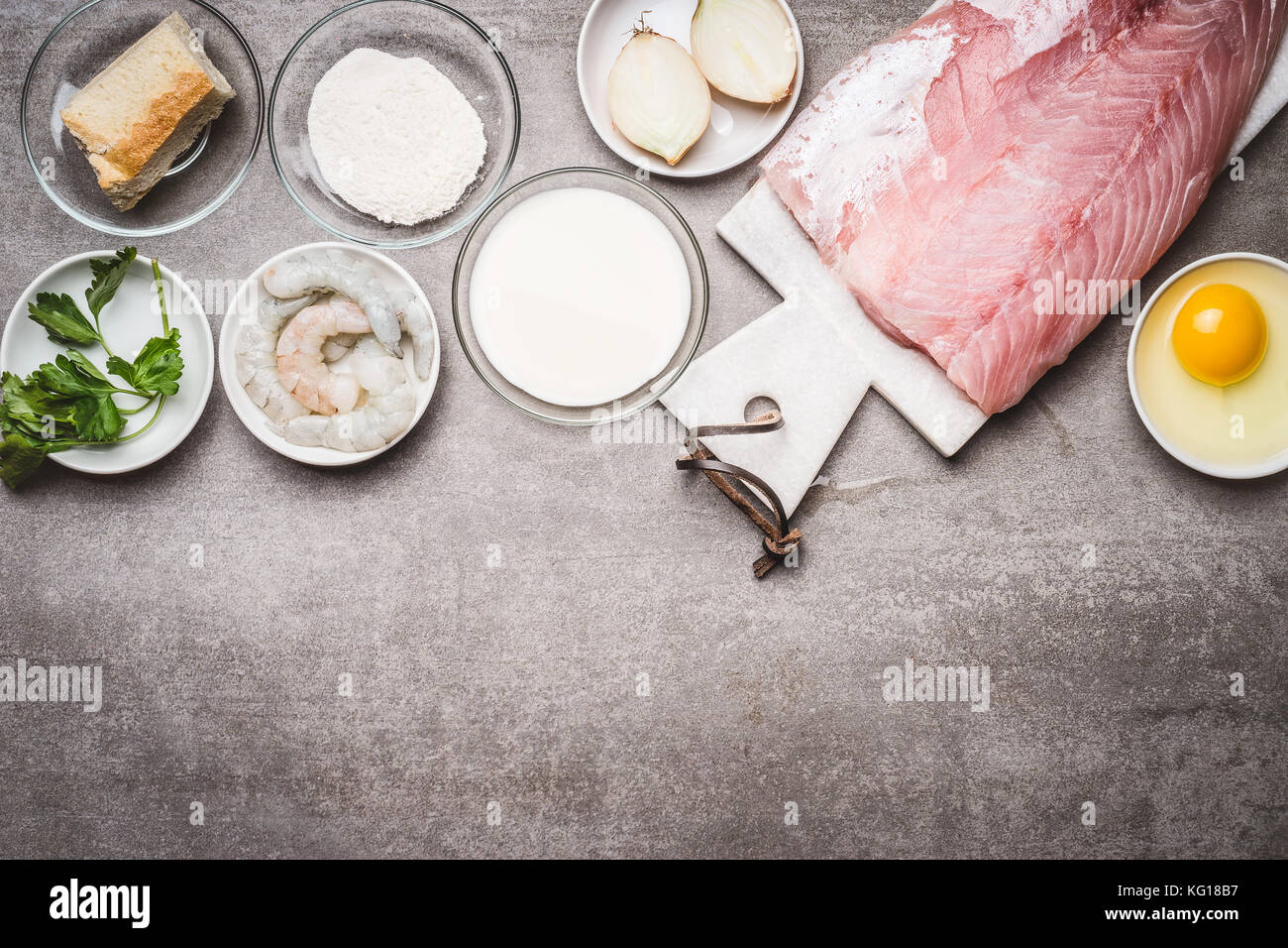 Fish patties cooking ingredients: raw fish fillets, egg,flour, soaked bread, shrimps, seasoning on concrete background, top view, border Stock Photo