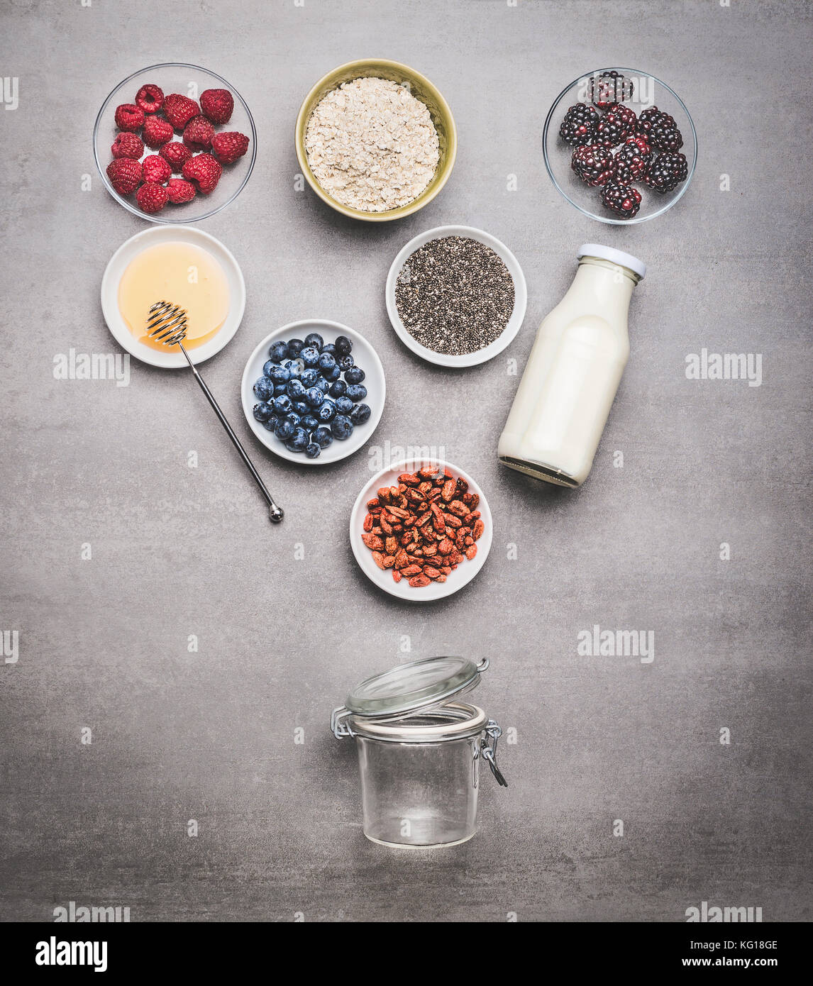 Healthy breakfast glass jar making with ingredients: chia seeds, goji berries, oatmeal , fresh berries , honey and milk or yogurt , top view, copy spa Stock Photo