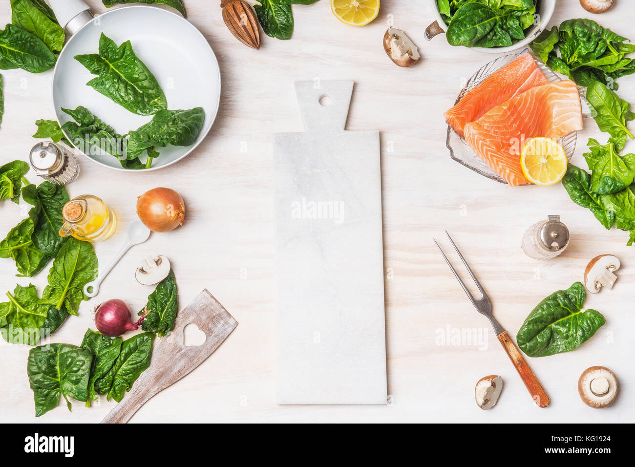 Healthy or diet  food background with cutting board, organic spinach leaves, salmon, pan ,fork and cooking ingredients on white kitchen table backgrou Stock Photo