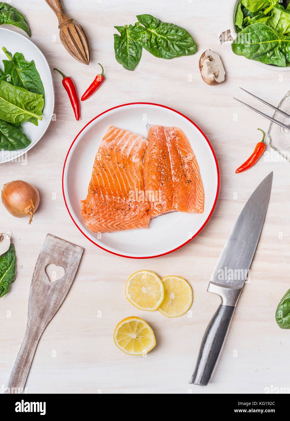 Raw salmon portion in bowl on white kitchen table background with cooking ingredients, spoon and knife, top view Stock Photo
