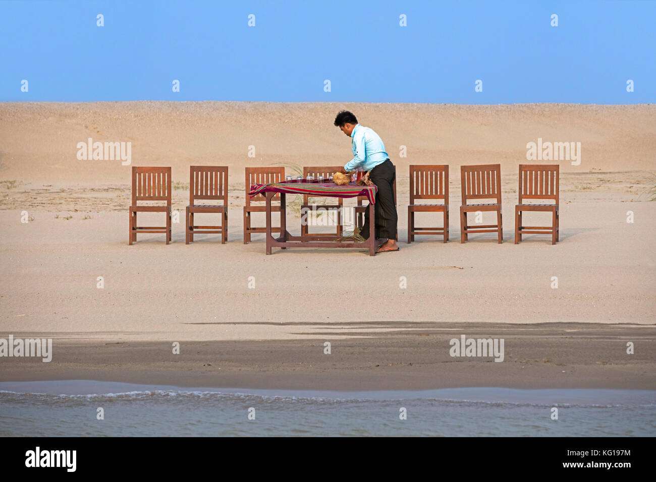 Burmese servant preparing dinner and setting the table for tourists at sunset along the Irrawaddy River / Ayeyarwady River in Myanmar / Burma Stock Photo