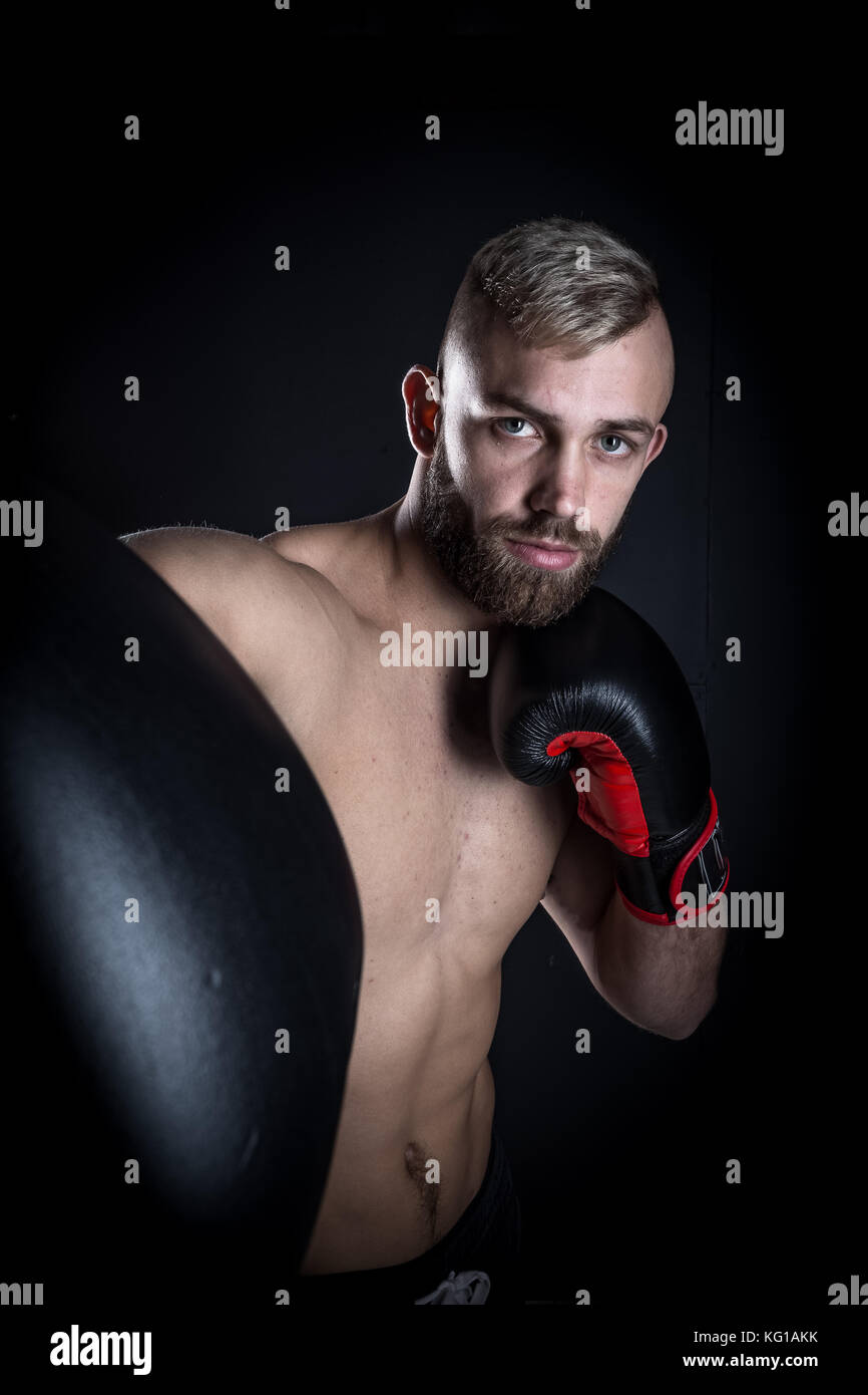 Male Athlete boxer punching a punching bag with dramatic edgy lighty in