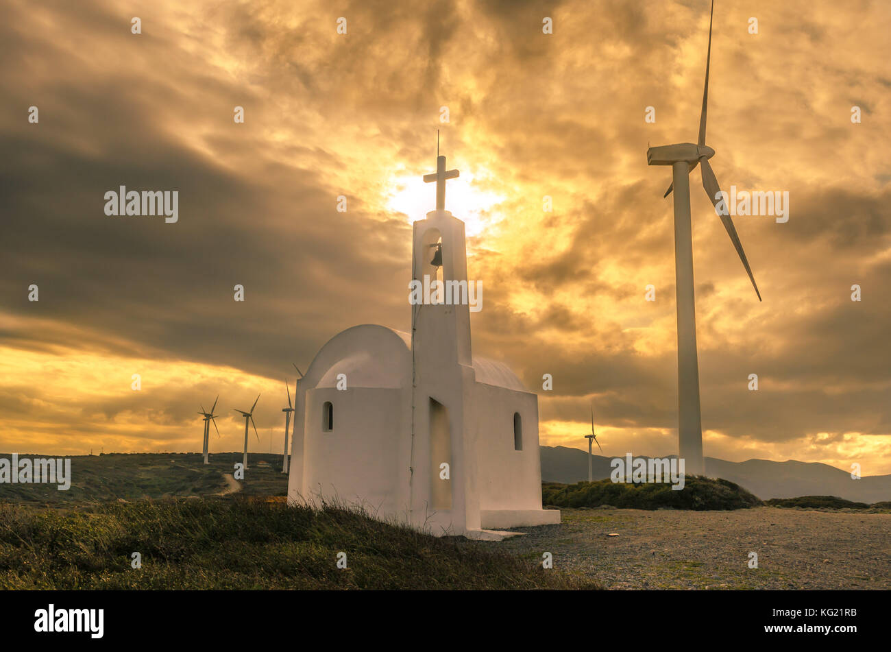 . amazing scene of a picturesque orthodox church surrounded by wind turbines at sunset time. Stock Photo