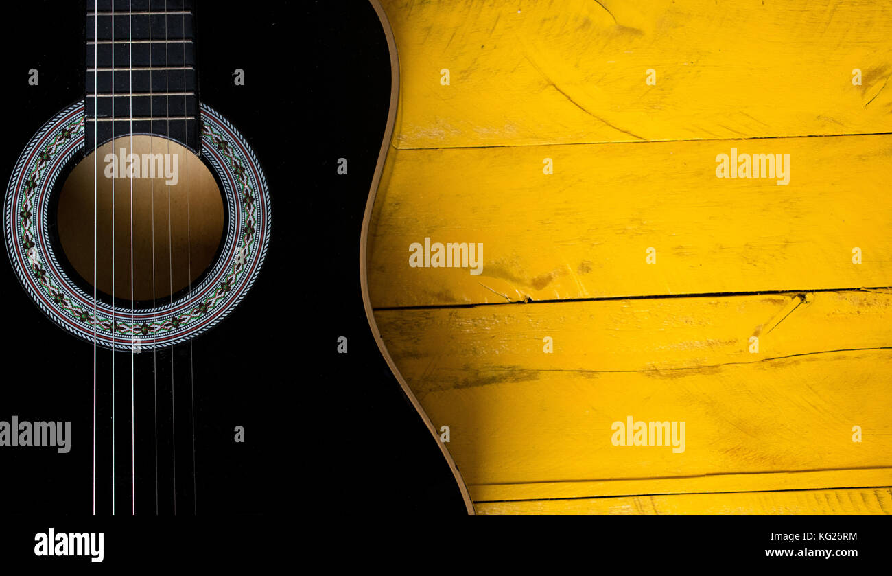Black Acoustic Guitar body closeup, vertical, on a yellow wood table