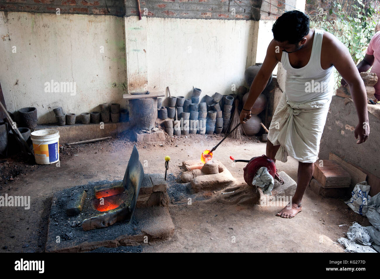 Man in white vest and dhoti, pouring molten bronze into clay mould, in Chola style lost wax bronze casting workshop, Thanjavur, Tamil Nadu, India Stock Photo