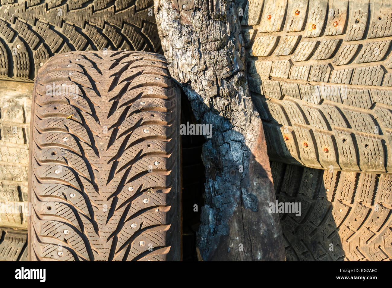 A stack of old tires with textured tread and charred plank on sunlight closeup Stock Photo