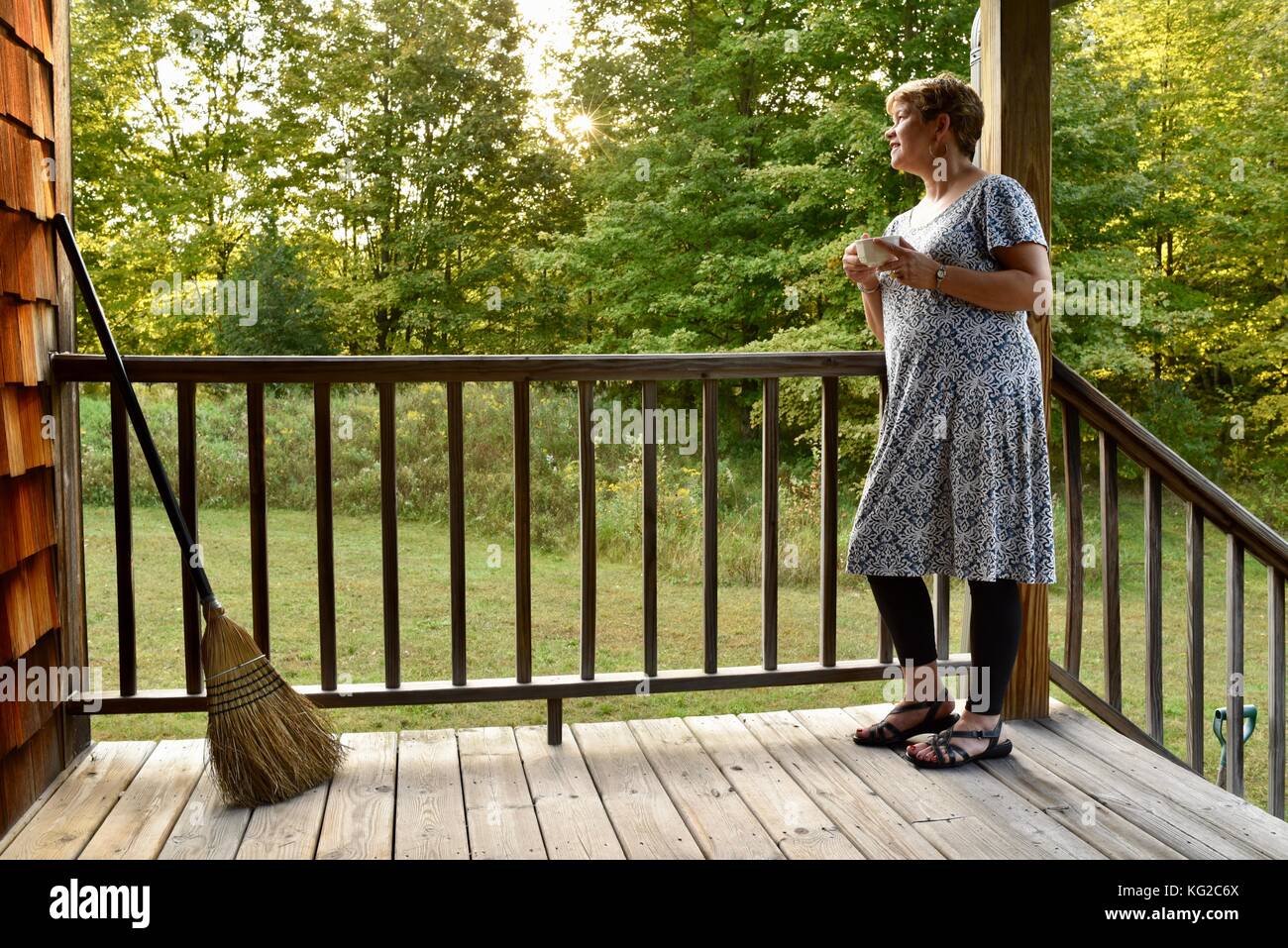 Middle-aged woman in dress on cabin porch with cup of coffee at sunrise ...