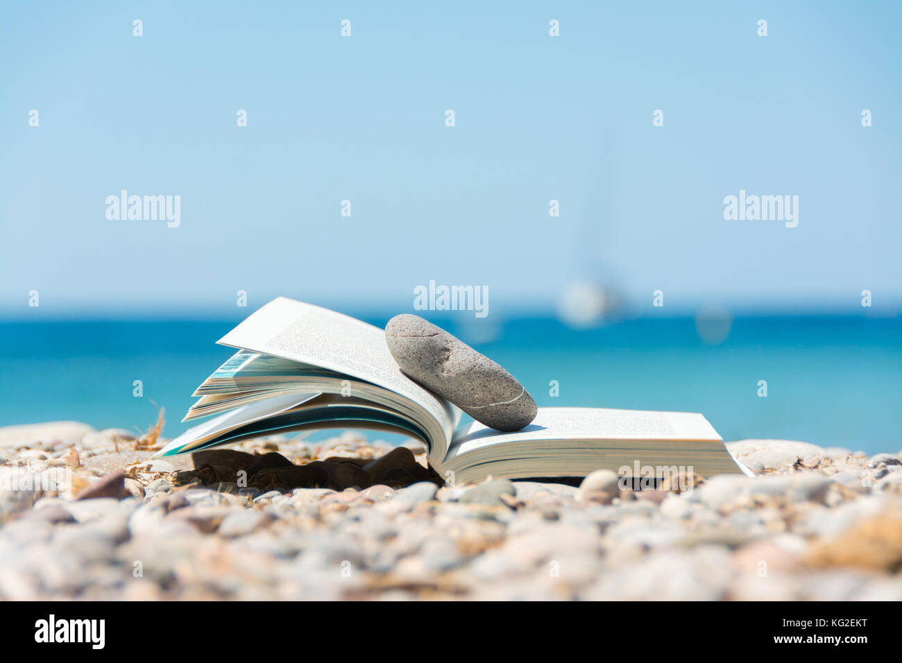 Reading in summer vacation, concept. Book on the pebble beach in Mallorca Stock Photo