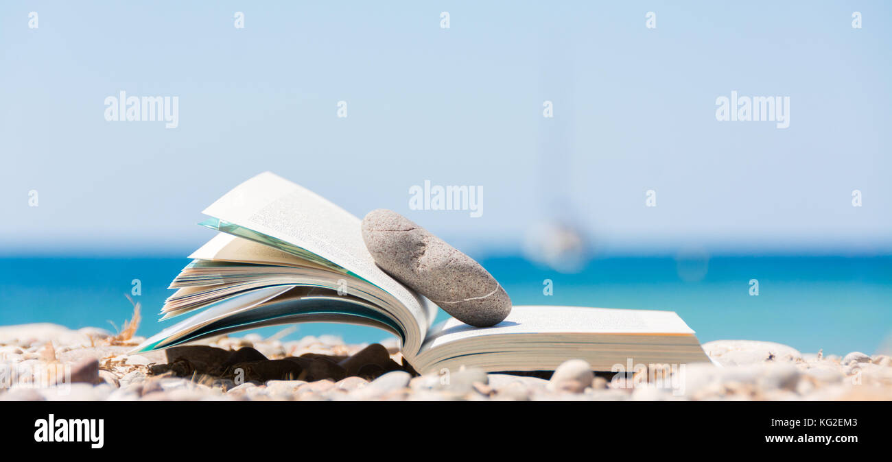 Reading in summer vacation, concept. Book on the pebble beach in Mallorca Stock Photo