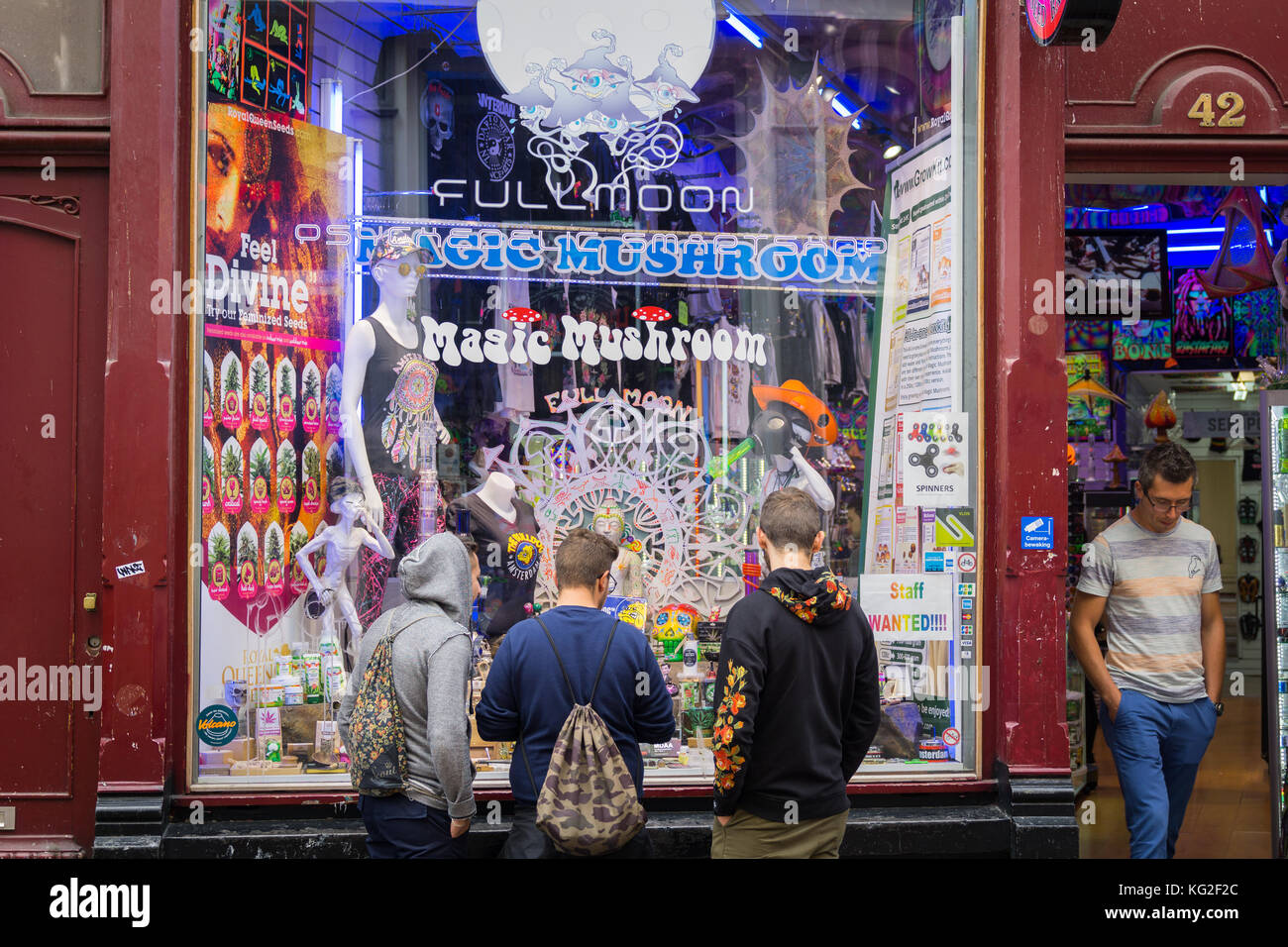 AMSTERDAM, HOLLAND - AUGUST 21, 2017; Three young guys window shop the display in shop selling range of psychedelic paraphenalia wihlie man stands in  Stock Photo