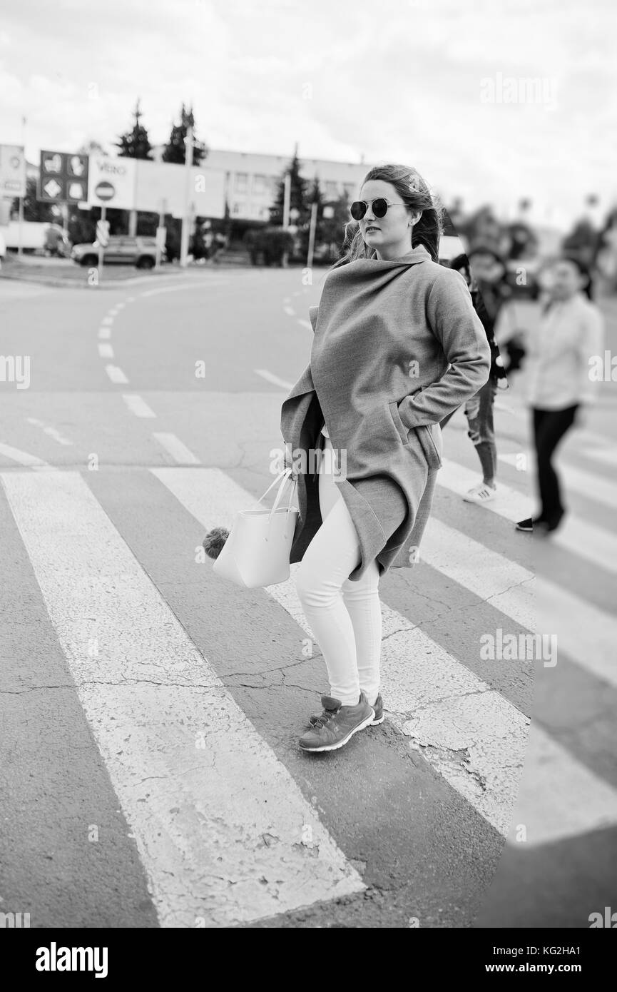 Girl in gray coat with sunglasses and handbag walking on the pedestrian crossing. Stock Photo