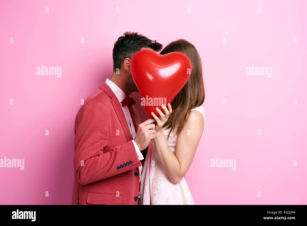 Affectionate couple covering face with balloon and kissing Stock Photo