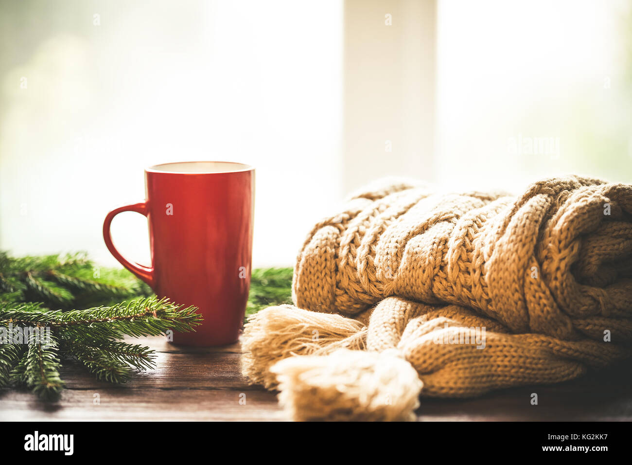 Christmas Hot Coffee in red cup on wooden table on a frosty winter day window background with knitted scarf and christmas tree branches. Home cozy hol Stock Photo