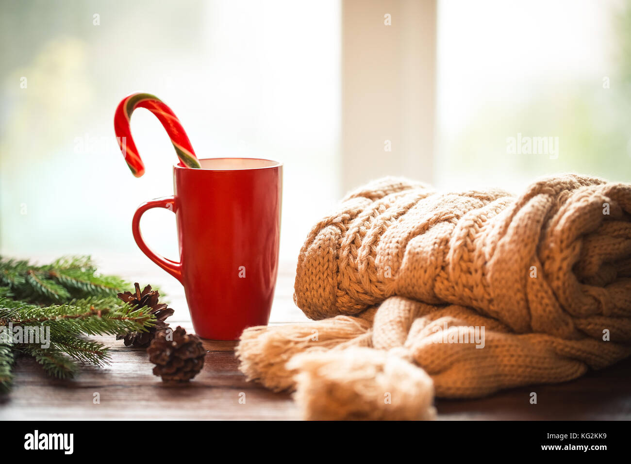 Christmas Hot Coffee in red cup on wooden table on a frosty winter day window background with knitted scarf, candy  and christmas tree branches. Home  Stock Photo
