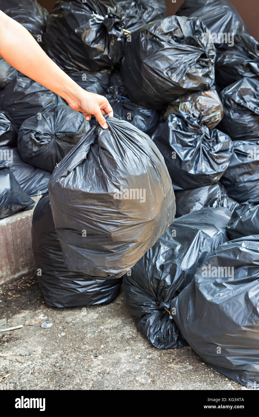 Hand carrying garbage bag over pile of garbage bags in a dump Stock