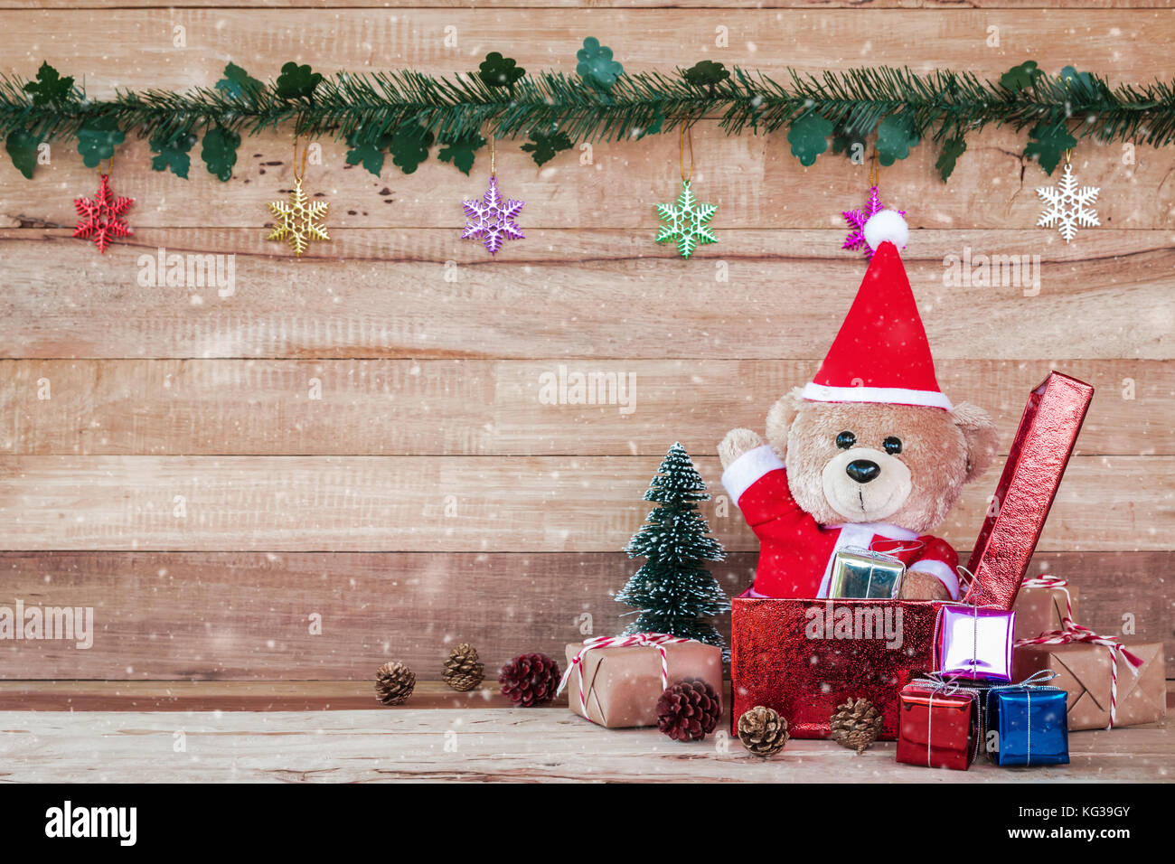 A photo of Teddy Bear in Santa Cross Dress Sitting in the middle of the enclave of Christmas decoration with woodboard background Stock Photo