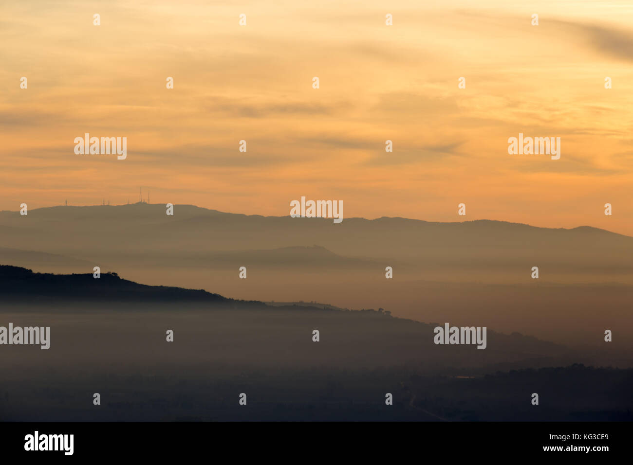 A valley filled by mist at sunset, with various layers of hills and mountains, and warm colors in the sky Stock Photo