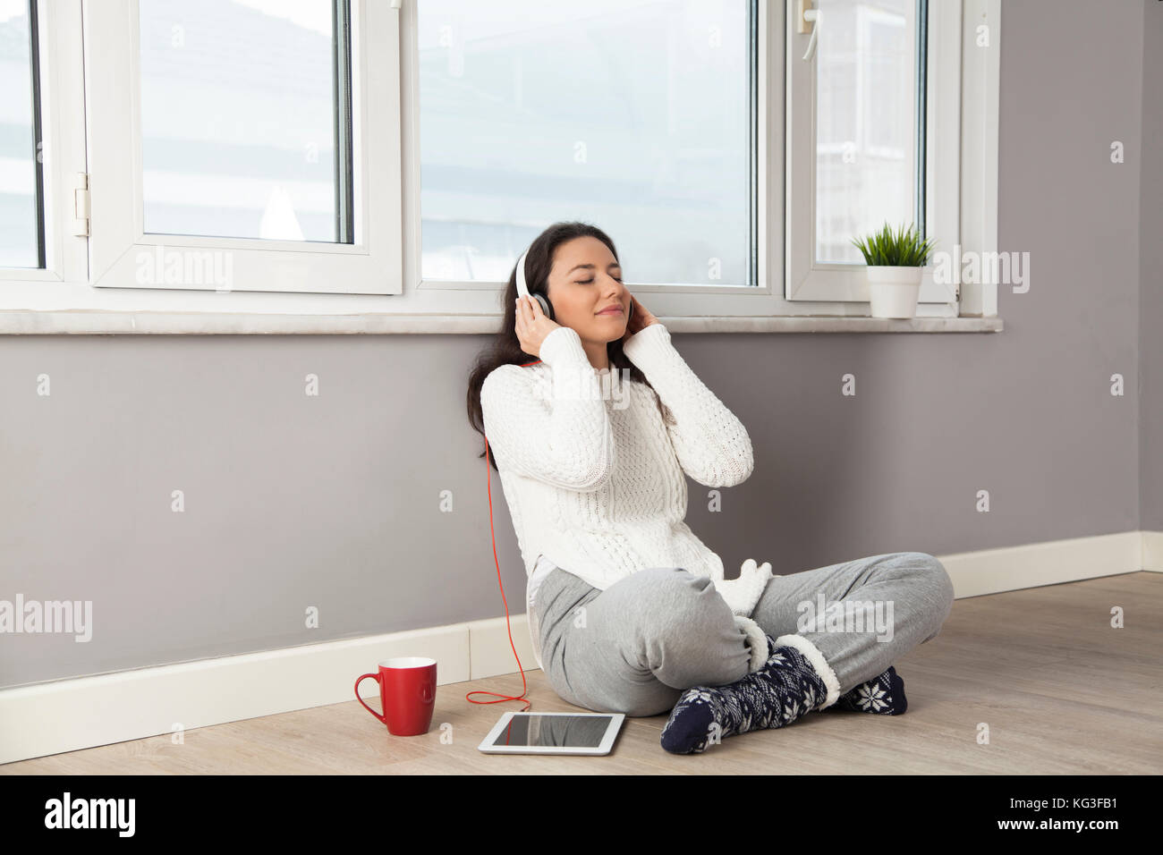 Happy young woman listening to music while sitting on the floor at home ...