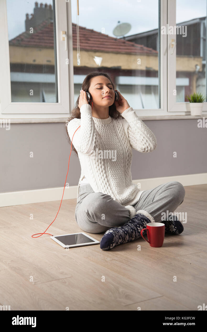 Happy young woman listening to music while sitting on the floor at home ...